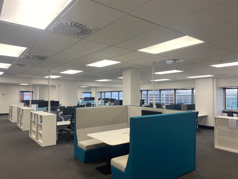 An open plan office space featuring desks with computer screens and a shared seating meeting booth.