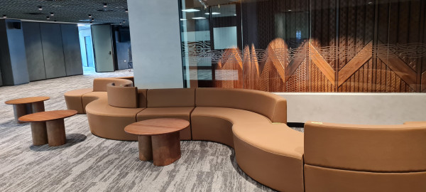 Light-brown soft seating curves and three brown round tables around an open office space.